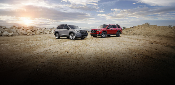 2025 Honda Passport and Honda Pilot front parked on rocky terrain with a cloudy sky background.